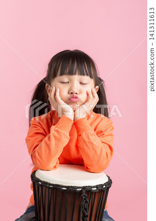 Thoughtful little girl resting her chin on her hands while sitting behind a djembe drum. Thoughtful little girl resting her chin on her hands while sitting behind a djembe drum. 141311613