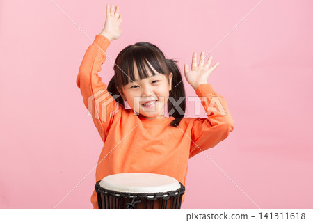Happy young girl raising her hands and smiling behind an African djembe drum in studio. Happy young girl raising her hands and smiling behind an African djembe drum in studio. 141311618