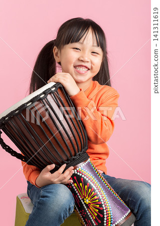 Cheerful young girl hugging a colorful patterned djembe drum and smiling widely at the camera. Cheerful young girl hugging a colorful patterned djembe drum and smiling widely at the camera. 141311619