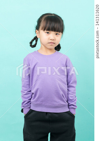Portrait of a casual little Asian girl standing with hands in pockets on a blue background. Portrait of a casual little Asian girl standing with hands in pockets on a blue background. 141311620