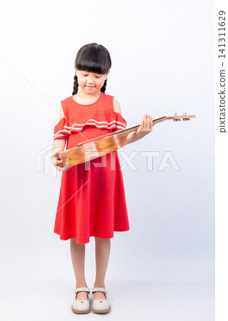 Happy little schoolgirl standing and laughing while holding a small wooden ukulele on white background. Happy little schoolgirl standing and laughing while holding a small wooden ukulele on white background. 141311629