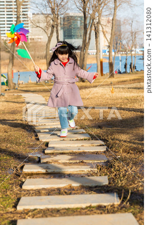 a lovely girl runs happily on the stone path in the park with a pinwheel. a lovely girl runs happily on the stone path in the park with a pinwheel. 141312080