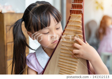 a beautiful young girl with a ponytail smiles while holding and playing a pipa. 141312113