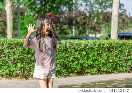 A young girl stands outdoors, making a playful, expressive pose with mouth open and hands raised. A young girl stands outdoors, making a playful, expressive pose with mouth open and hands raised. 141312147
