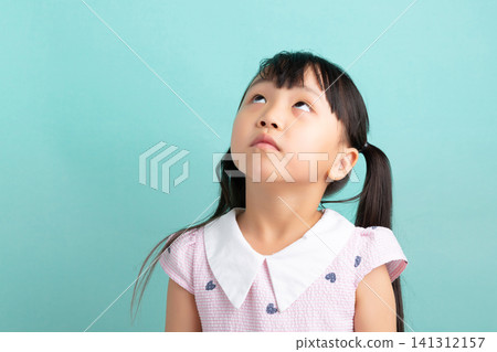 Curious young child looking up thoughtfully against a solid turquoise wall in a studio. 141312157
