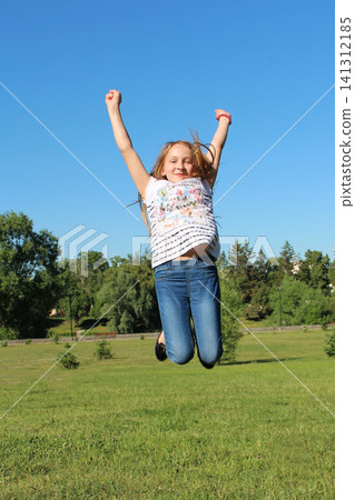 Happy young girl jumping high with hands up in a green summer park Happy young girl jumping high with hands up in a green summer park 141312185