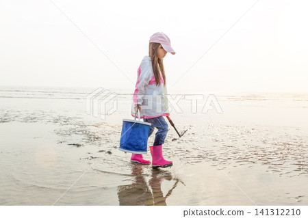 Full length of a young girl holding a blue bucket and walking on a vast mudflat at low tide. 141312210
