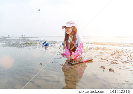 Happy young girl looking away while digging for shells in the mudflats during low tide. 141312216