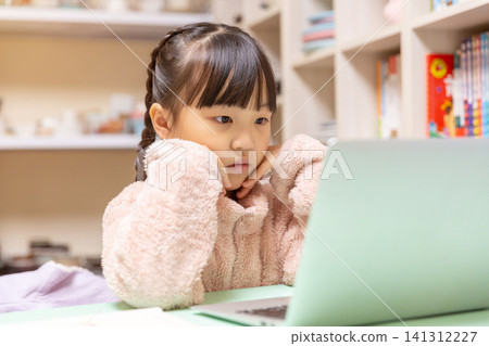 Focused girl looking attentively at a laptop screen during an online school class at home. 141312227