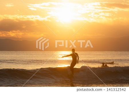 Surfing in the ocean shimmering in the colors of the setting sun at Kugenuma Beach, Shonan. Surfing in the ocean shimmering in the colors of the setting sun at Kugenuma Beach, Shonan. 141312542