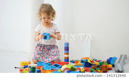 Little girl concentrating as she tries to connect and join pieces of colorful construction blocks while sitting on the floor. Childhood learning concept Little girl concentrating as she tries to connect and join pieces of colorful construction blocks while sitting on the floor. Childhood learning concept 141312640
