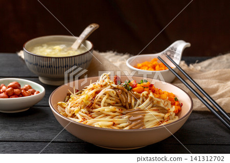 a bowl of traditional Wuhan hot dry noodles with sesame paste, peanuts and pickles on a wooden tray 141312702