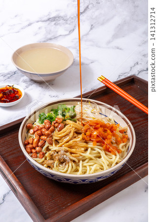 drizzling spicy red chili oil with a spoon onto traditional Wuhan hot dry noodles, high angle view drizzling spicy red chili oil with a spoon onto traditional Wuhan hot dry noodles, high angle view 141312714