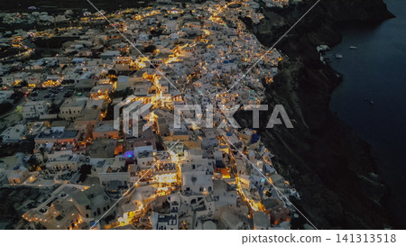 Horizontal aerial view of the famous Oia village in Santorini Greece at night with warm city lights glowing on high volcanic caldera cliffs against dark Aegean Sea Horizontal aerial view of the famous Oia village in Santorini Greece at night with warm city lights glowing on high volcanic caldera cliffs against dark Aegean Sea 141313518