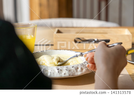A hand holding a silver fork eating creamy mashed potatoes with melted cheese from a rustic ceramic bowl, capturing a cozy home meal dining experience during a bright sunny morning A hand holding a silver fork eating creamy mashed potatoes with melted cheese from a rustic ceramic bowl, capturing a cozy home meal dining experience during a bright sunny morning 141313578
