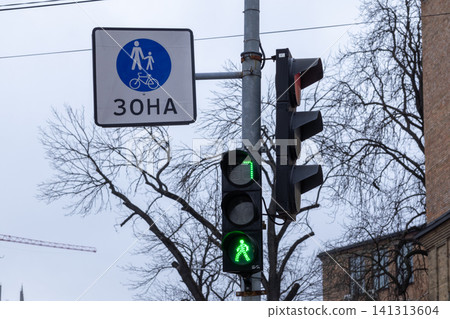 A pedestrian zone traffic sign and illuminated green light for people crossing a city street, conveying urban safety regulations and active mobility infrastructure in a modern center A pedestrian zone traffic sign and illuminated green light for people crossing a city street, conveying urban safety regulations and active mobility infrastructure in a modern center 141313604
