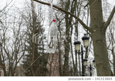 An empty plastic bottle hangs from a leafless tree branch in a park, highlighting environmental awareness and the urgent need for recycling to combat urban pollution and litter waste An empty plastic bottle hangs from a leafless tree branch in a park, highlighting environmental awareness and the urgent need for recycling to combat urban pollution and litter waste 141313605