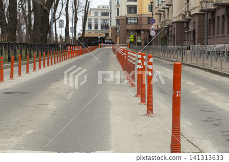 Orange reflective traffic delineators line a city street, effectively separating vehicle lanes to enhance road safety and manage efficient urban transport flow for local commuters Orange reflective traffic delineators line a city street, effectively separating vehicle lanes to enhance road safety and manage efficient urban transport flow for local commuters 141313633