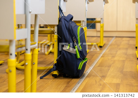 A blue schoolbag hangs on a chair in an empty primary school classroom, conveying the anticipation of learning and a return to education for children in a bright modern setting A blue schoolbag hangs on a chair in an empty primary school classroom, conveying the anticipation of learning and a return to education for children in a bright modern setting 141313742