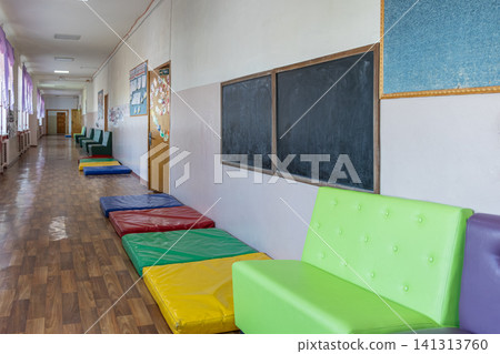 An empty school corridor features colorful floor mats and green cushioned seating along white walls, reflecting a bright and welcoming educational environment for young students An empty school corridor features colorful floor mats and green cushioned seating along white walls, reflecting a bright and welcoming educational environment for young students 141313760