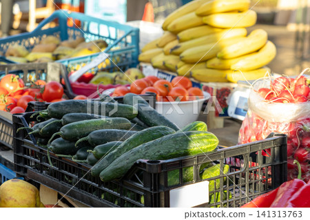 Fresh cucumbers in black plastic crates at an outdoor farmers market, showcasing ripe vegetables and fruits displayed for sale, conveying healthy nutrition and local agriculture 141313763