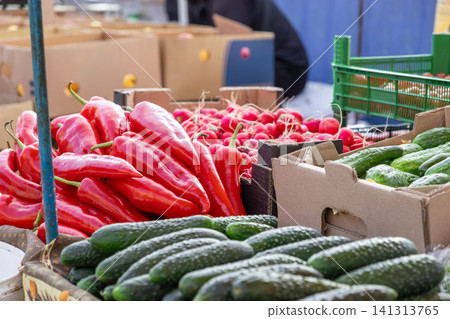 Fresh red peppers, radishes, and green cucumbers are neatly arranged in cardboard crates at a local outdoor farmers market to showcase seasonal organic produce for healthy nutrition Fresh red peppers, radishes, and green cucumbers are neatly arranged in cardboard crates at a local outdoor farmers market to showcase seasonal organic produce for healthy nutrition 141313765