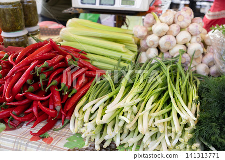 Fresh red chili peppers with green onions and celery sticks displayed on a market stall table, highlighting vibrant seasonal produce for healthy organic cooking and culinary themes Fresh red chili peppers with green onions and celery sticks displayed on a market stall table, highlighting vibrant seasonal produce for healthy organic cooking and culinary themes 141313771
