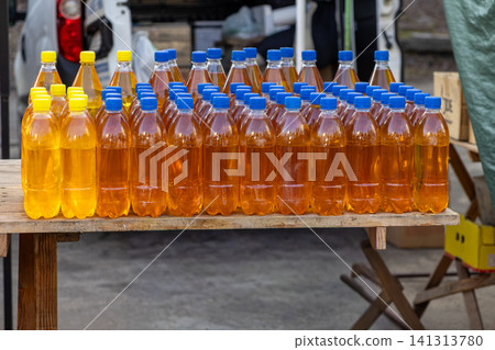 Rows of plastic bottles filled with golden juice or tea displayed on a rustic wooden table at an outdoor market stall representing local production and fresh natural refreshments Rows of plastic bottles filled with golden juice or tea displayed on a rustic wooden table at an outdoor market stall representing local production and fresh natural refreshments 141313780