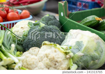 Fresh broccoli and cauliflower heads displayed with assorted garden vegetables at an outdoor market stall, highlighting healthy organic produce for a balanced natural diet and nutrition Fresh broccoli and cauliflower heads displayed with assorted garden vegetables at an outdoor market stall, highlighting healthy organic produce for a balanced natural diet and nutrition 141313785