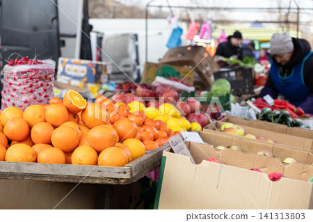 Fresh oranges and assorted produce displayed on a wooden table at an outdoor street market, highlighting local harvest commerce and seasonal nutrition in a busy retail setting 141313803