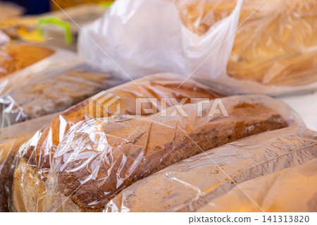 Fresh loaves of dark artisan rye bread wrapped in clear plastic bags, displayed on a bakery counter to convey traditional food production, healthy nutrition, and daily retail trade Fresh loaves of dark artisan rye bread wrapped in clear plastic bags, displayed on a bakery counter to convey traditional food production, healthy nutrition, and daily retail trade 141313820