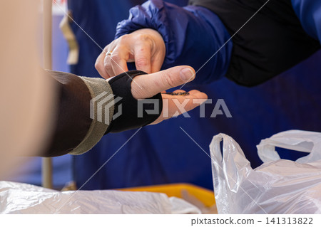 A person wearing a black orthopedic wrist brace receives a small item from another hand outdoors, symbolizing careful interaction, injury recovery support, or commerce assistance A person wearing a black orthopedic wrist brace receives a small item from another hand outdoors, symbolizing careful interaction, injury recovery support, or commerce assistance 141313822