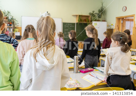 Students stand in a bright elementary school classroom during a lesson, observing the blackboard with focus to represent the daily academic environment and early childhood education Students stand in a bright elementary school classroom during a lesson, observing the blackboard with focus to represent the daily academic environment and early childhood education 141313854
