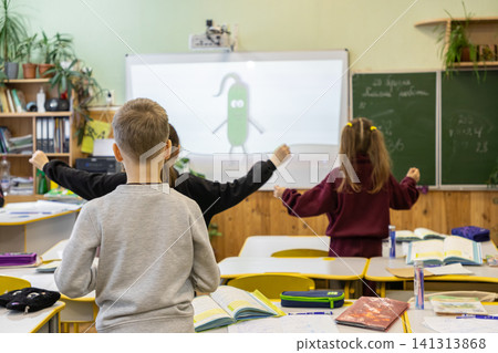 Elementary students stretch their arms in a bright classroom during a break while watching an interactive lesson on a projector to promote physical wellness and healthy habits Elementary students stretch their arms in a bright classroom during a break while watching an interactive lesson on a projector to promote physical wellness and healthy habits 141313868