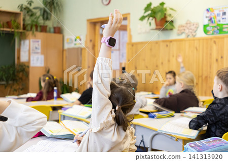 A young schoolchild raises their hand in a primary school classroom to answer a question, representing active participation and engagement within a traditional learning environment A young schoolchild raises their hand in a primary school classroom to answer a question, representing active participation and engagement within a traditional learning environment 141313920