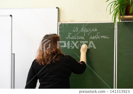 A dedicated teacher writes a complex math equation on a green chalkboard in an elementary classroom, demonstrating academic guidance and pedagogical support for young students A dedicated teacher writes a complex math equation on a green chalkboard in an elementary classroom, demonstrating academic guidance and pedagogical support for young students 141313923