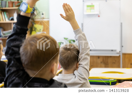 Students raising hands in an elementary school classroom during a lesson, conveying active engagement, academic curiosity, and eager participation in the daily primary school routine Students raising hands in an elementary school classroom during a lesson, conveying active engagement, academic curiosity, and eager participation in the daily primary school routine 141313928