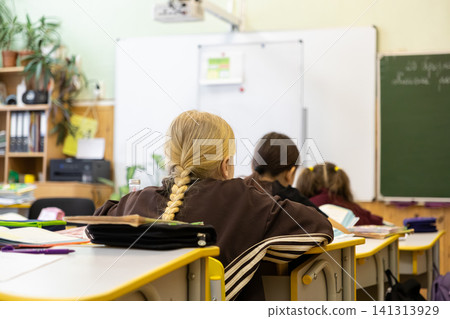 Students sit at desks in a bright elementary classroom during a lesson, observing the whiteboard with focus while engaged in a productive and structured modern academic environment Students sit at desks in a bright elementary classroom during a lesson, observing the whiteboard with focus while engaged in a productive and structured modern academic environment 141313929