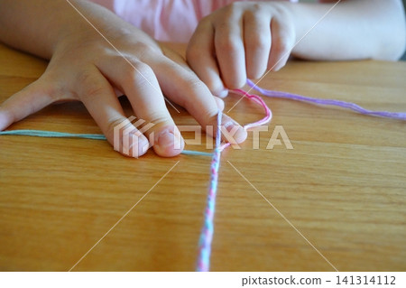 A child's hands and crafting process as they knit friendship bracelets with colorful yarn. A child's hands and crafting process as they knit friendship bracelets with colorful yarn. 141314112