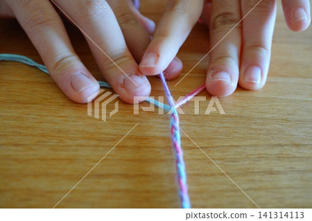 The child's fingertips and colorful yarn are focused on making friendship bracelets. The child's fingertips and colorful yarn are focused on making friendship bracelets. 141314113