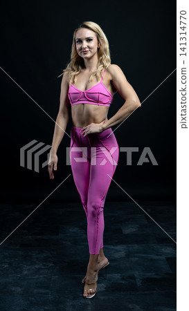 Confident fitness model posing in pink sportswear on black background Confident fitness model posing in pink sportswear on black background 141314770