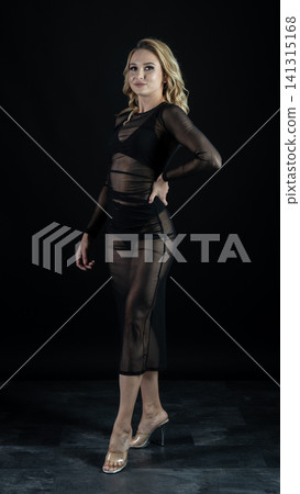 Young blonde dancer wearing transparent black dress and high heels posing in studio with black background Young blonde dancer wearing transparent black dress and high heels posing in studio with black background 141315168