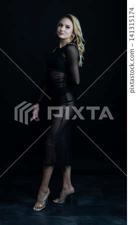 Young blonde dancer wearing transparent black dress and high heels posing in studio with black background Young blonde dancer wearing transparent black dress and high heels posing in studio with black background 141315174