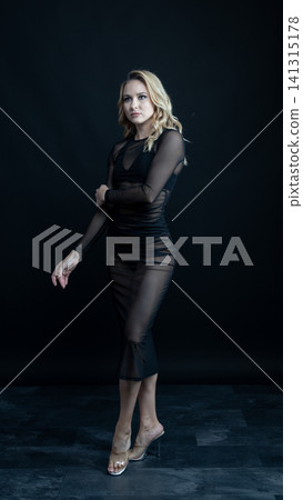 Young blonde dancer wearing transparent black dress and high heels posing in studio with black background Young blonde dancer wearing transparent black dress and high heels posing in studio with black background 141315178