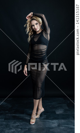 Young blonde dancer wearing transparent black dress and high heels posing in studio with black background Young blonde dancer wearing transparent black dress and high heels posing in studio with black background 141315187