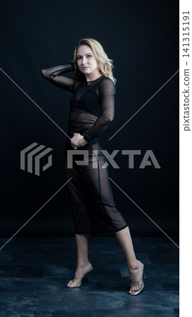 Young blonde dancer wearing transparent black dress and high heels posing in studio with black background Young blonde dancer wearing transparent black dress and high heels posing in studio with black background 141315191