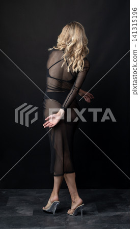 Young blonde dancer wearing transparent black dress and high heels posing in studio with black background Young blonde dancer wearing transparent black dress and high heels posing in studio with black background 141315196