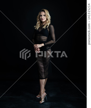 Young blonde dancer wearing transparent black dress and high heels posing in studio with black background Young blonde dancer wearing transparent black dress and high heels posing in studio with black background 141315214