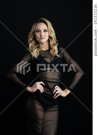 Young blonde dancer wearing transparent black dress and high heels posing in studio with black background Young blonde dancer wearing transparent black dress and high heels posing in studio with black background 141315216