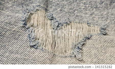 Close-up of a torn hole in jeans fabric Close-up of a torn hole in jeans fabric 141315282